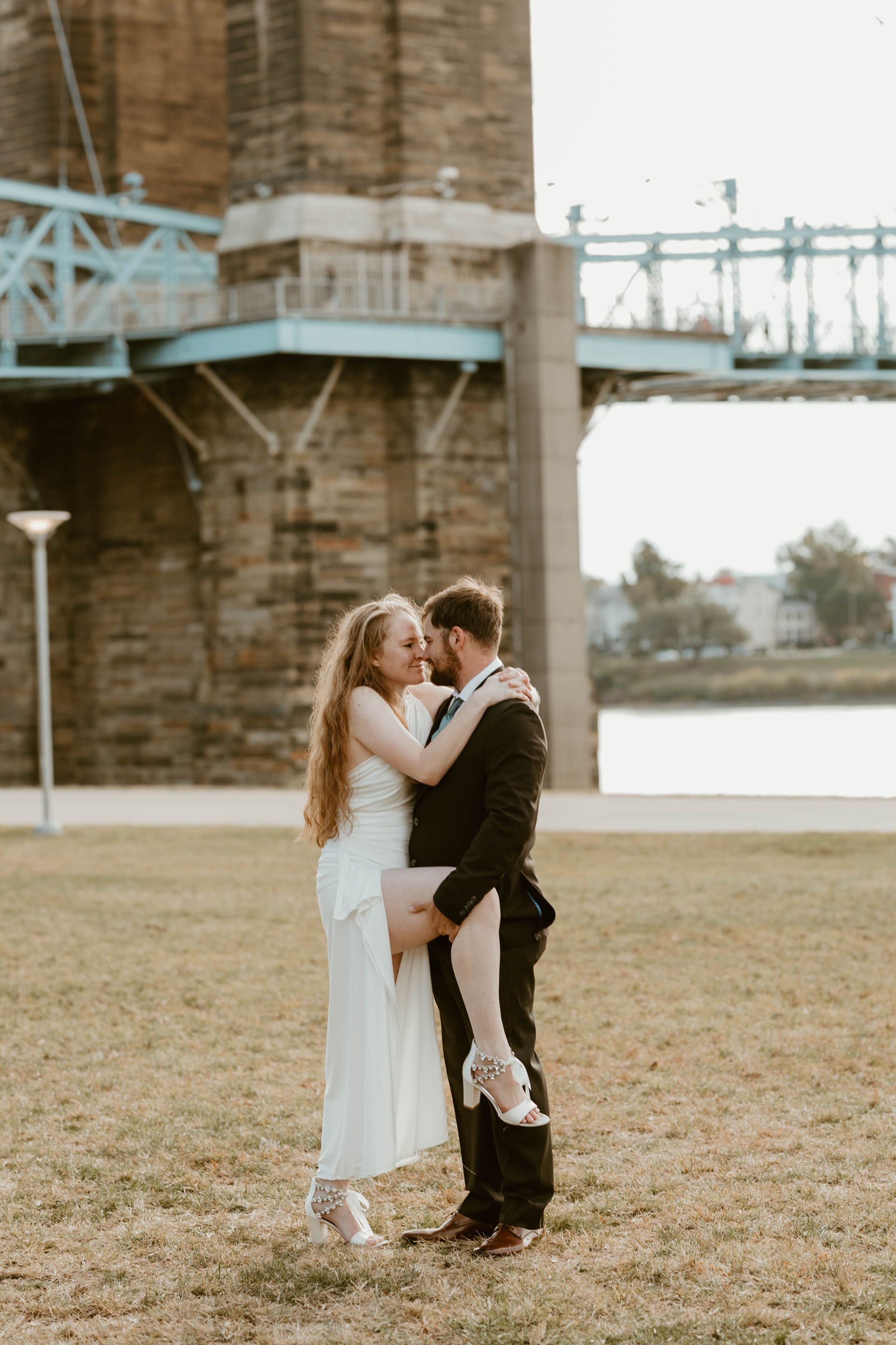 Couple embracing under the Roebling Bridge at golden hour